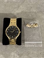 Full view of gold-tone watch on black cushion with extra bracelet links in plastic bag