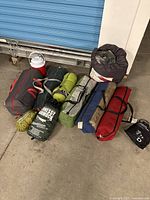 Wide view showing all camping items including tents in bags, sleeping bags, hammock bag, and cooler jug