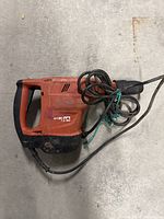 Overall view of drill laid on concrete floor showing handle, body and power cord.