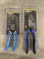 Photo of two Klein Tools pliers in sealed packaging on a concrete floor: a Heavy-Duty Wire Stripper-Crimper and Lineman's Pliers.