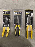 Three Klein Tools hand tools in packaging: cable stripper/cutter, side cutting long nose pliers, and lineman's pliers.