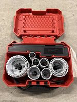 Top view of open red carrying case with eight white hole saws of varying diameters inside.