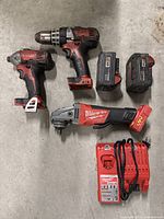 Overhead shot of drill, impact driver, angle grinder, two batteries and charger on concrete floor