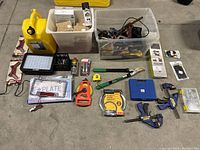 Overview of assorted tools including a yellow plastic jerry can, LED light panel, clamps, measuring wheels, license plate frame, and hardware boxes.