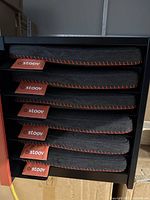 Stacked new Stoov heated seat cushions showing the grey fabric with red stitching and red tags.