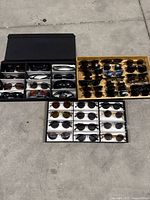 Three trays of assorted sunglasses laid out on concrete floor