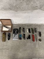 Full lineup of items laid out on the floor including hatchet, sheath, multiple folding knives, boxed razor, lighters, and other small objects.