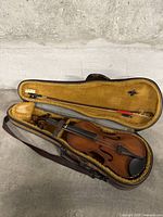 Violin inside open brown hard case with yellow interior, showing front of violin and bow inside lid