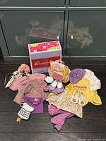 Lot displayed with My American Girl box, various doll clothes and knitwear including a sweater, skirt, leggings, cardigan, hat, and accessories like shoes and backpack.