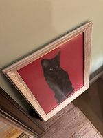 Angled view of framed black cat drawing leaning against wall.