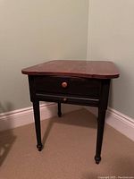 Front view of the black side table with varnished wood top, showing the drawer and base.