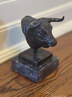 Front-left three-quarter view of bronze bull head on marble base showing horn curvature and fur texture.