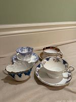 Front perspective view showing three tea cups with matching saucers and cream jug, emphasizing patterns and colors.