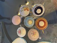 Top-down view of seven assorted teacups displaying fruit, floral, pink, blue, cobalt, burgundy and aqua patterns