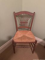 Front view of a wooden chair with woven rattan seat and lyre-shaped backrest, showing wear and usage marks.