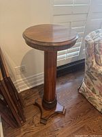 Front angle view of the round wooden pedestal table showing the smooth round top, central column, and carved base with three feet.