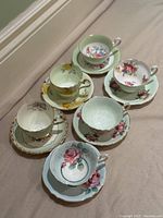 Full set of six tea cups and saucers arranged showing pastel colors and floral patterns.