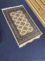 Full view of the wool accent rug placed on blue carpet, showing the rectangular shape and overall pattern.