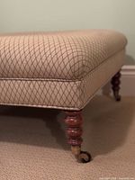 Close-up of one corner showing beige diamond-patterned upholstery, turned wooden leg and brass caster wheel