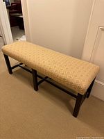 Side-angle view of bench showing dark wooden frame and beige patterned seat