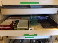 Drawer with multiple bakeware dishes including ceramic dishes with red exterior and white interior, green ceramic dish, and clear glass dishes in different sizes and shapes.