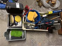 Overview of assorted car supplies including sponges, brushes, jumper cables, and Simoniz polisher in black case