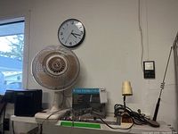 Photo of lot showing the desk fan, Cobra 7 Ultra CB radio box, antenna, small heater, desk lamp, and wall clock on a white shelf against a wall.