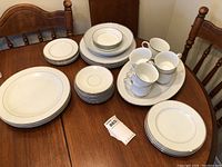 Set of white china with silver rim arranged on wooden table showing plates, bowls, cups, and platters including the Nitto and Royal Norfolk pieces.