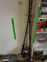 Four assorted fishing poles standing upright against a wall, showing the full length including reels attached to some poles.