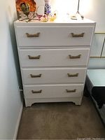 Full front view of the white painted 5-drawer highboy dresser with brass-tone handles, showing condition and size in a corner of a room.