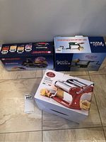 Lot showing all three boxed kitchen gadgets: Starfrit Mandoline slicer, Apple Peeler, and Remy Oliver Pasta Machine