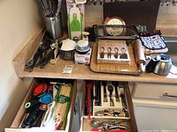 Photo of kitchen countertop and drawers with various utensils, cutlery, chopping tools, linens, and kitchen gadgets.