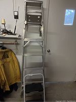 Photo showing the aluminum step ladder leaning against a wall with the small two-step step stool placed in front of it, both exhibiting wear.