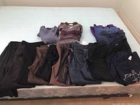 Lot of ladies pants, yoga pants, jeans, sweatshirts, and sweaters laid on mattress bed showing color variety and style.