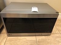 Closed front view of LG microwave with stainless steel and black reflective glass door, model label visible.