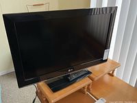 LG 32 inch TV with its remote control placed on wooden table.