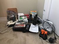 Overview of all items including CD player, Blu-ray player, telephones, walkie talkies, and camera film envelopes arranged on a carpeted floor against a wall.