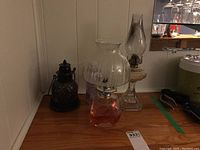 Overall view of the two oil lamps, tea light lamp, and fuel placed on a wooden surface against a wall.