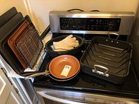 Full view of stove with all ovenware including roasting pan, frying pans, baking sheets, and racks.