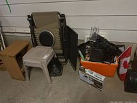 Overview of lot showing zero gravity lounge chair, plastic patio tables, small wooden shelf, orange cooler tub, and Canadian flag nearby.