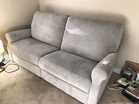 Front-side view of the light greenish electric reclining sofa placed against a wall, showing the soft fabric upholstery and cushions.