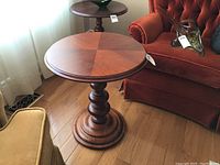 Full view of the round side table beside a red chair and near a window showing its shape, base, and top.