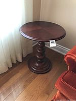 Full view of round side table next to window and chair, showing table top and overall shape.