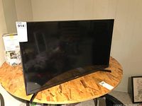 Full front angled view of the Samsung curved flat screen TV on a round wooden table.