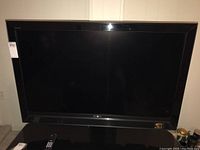 Wide front view of Sony TV mounted on smoked glass stand, remote visible on stand.