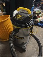 Stanley wet and dry vacuum with attached hose and orange bucket beside it in a garage setting.