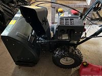 Side view of black Yardworks snowblower with plastic chute and pneumatic tire, red jerry can visible