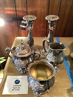 Full view of all five pieces on a wooden table, showing the teapot, sugar dish, creamer, bowl, and two candlesticks.