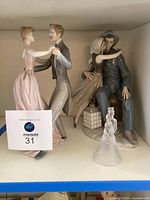 Three figurines on shelf: dancing couple, sitting couple, and a small crystal bell figure all displayed together