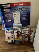 Photo showing assembled lot with First Alert carbon monoxide alarm box and various fire extinguisher boxes including Kidde brand.